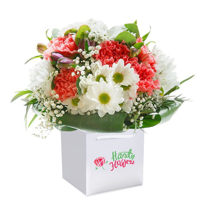 Elegantly presented in a flawless white square gift bag, this dazzling bouquet showcases the skill and creativity of Marks Gate florists. Blushing coral and gentle peach carnations unfurl in plush, ruffled layers, sending forth a subtle, sweetly floral scent that hints at home gardens in the area. Scattered amid this opulent display are crisp white daisies with lively green-gold centers, infusing the bouquet with freshness reminiscent of sunny days in local playgrounds and parks. Filigree sprays of delicate white baby's breath add a light, cloudlike softness, while modest, purple-tinged buds nestled along one side introduce an intriguing note of anticipation. Each bloom and leaf is nestled within a verdant frame of deep green foliage; the broad, shiny leaves cradle the bouquet, evoking the sheltering canopy of trees that line the neighbourhood. White satin ribbon handles arch gracefully at the top of the bag, designed for seamless, stylish delivery throughout Marks Gate-ideal for celebrations on the green or heartfelt gestures at home. Captured against an immaculate white background, the arrangement's vitality and beauty are accentuated, making the flowers leap to the eye. Perfect for birthdays, anniversaries, or spontaneous acts of kindness, this bouquet captures the inclusive spirit and bright optimism of Marks Gate with every blossom.